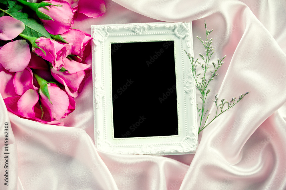 the Empty photo frame with a bouquet sweet pink roses  petal on  soft pink silk fabric , romance and