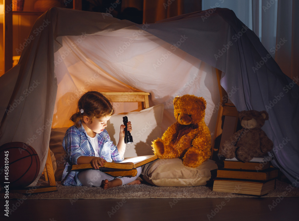 睡前带着书、手电筒和泰迪熊的小女孩。