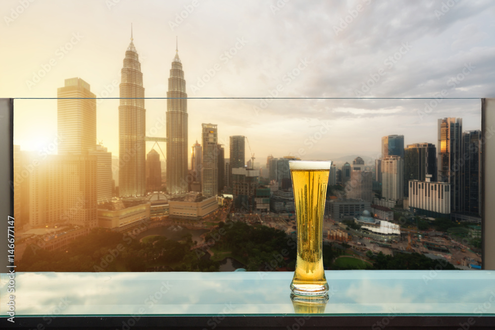 屋顶酒吧的桌子上放着啤酒和泡沫啤酒，背景是吉隆坡的摩天大楼。