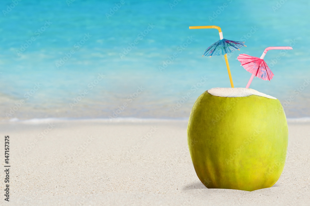 热带沙滩上的绿色椰子夏日鸡尾酒，背景是蓝色的海水。