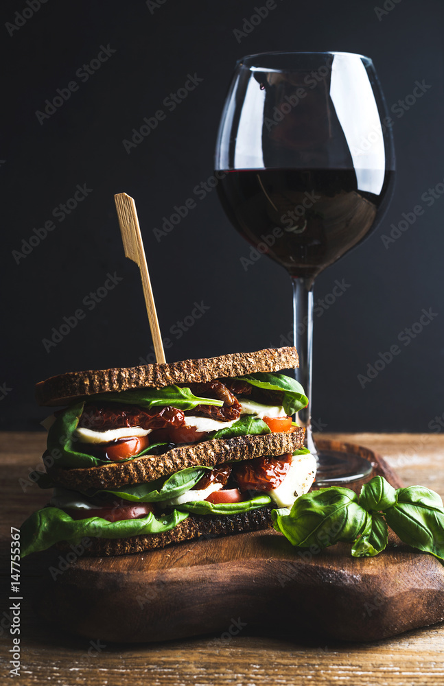 自制caprese三明治和一杯红酒放在木板上，深色背景，选择性聚焦，v