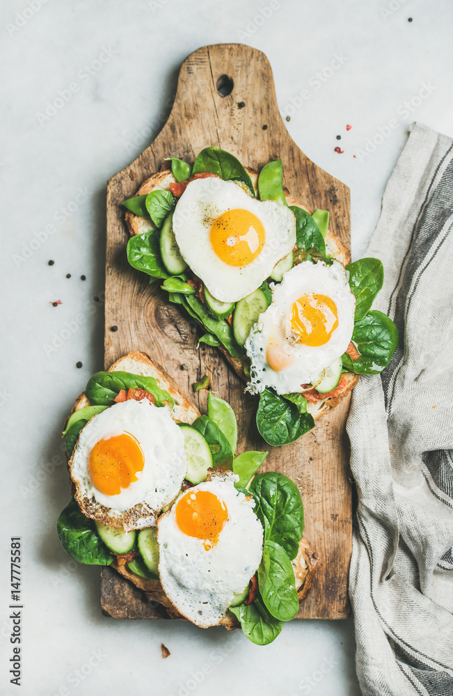 健康早餐三明治。面包烤面包配煎蛋和新鲜蔬菜，放在木板上
