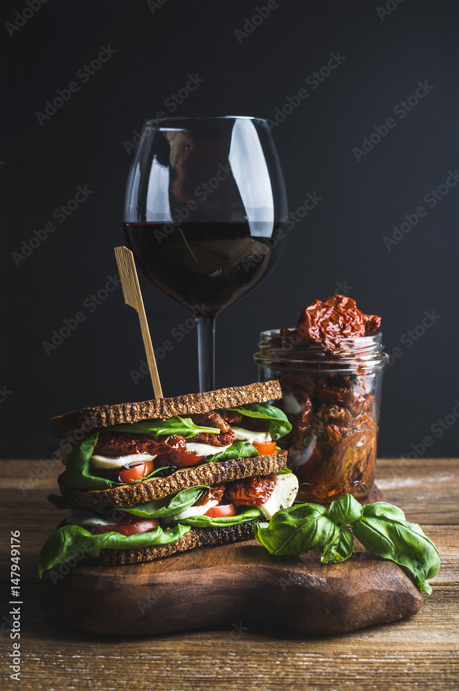 自制caprese三明治，一杯红酒和干番茄，装在木板上的罐子里，深色backgro