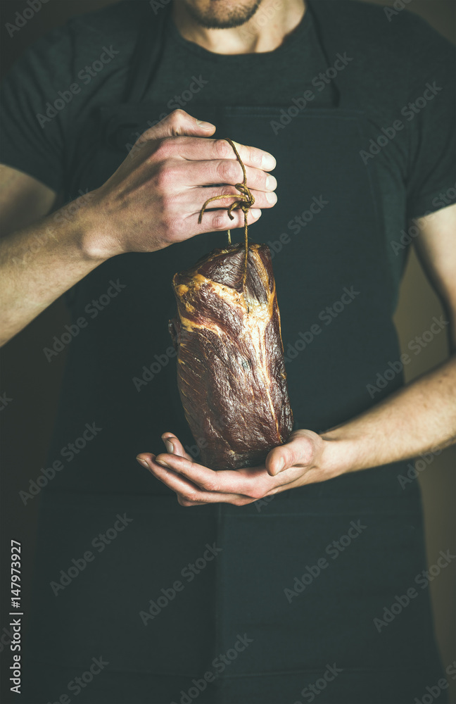 在当地农贸市场，一名身穿黑色围裙的男子手里拿着一块腌猪肉。Gourmet，org