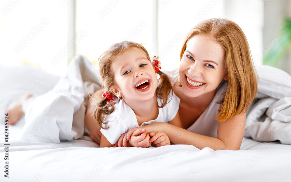 幸福的家庭母亲和孩子女儿在床上大笑