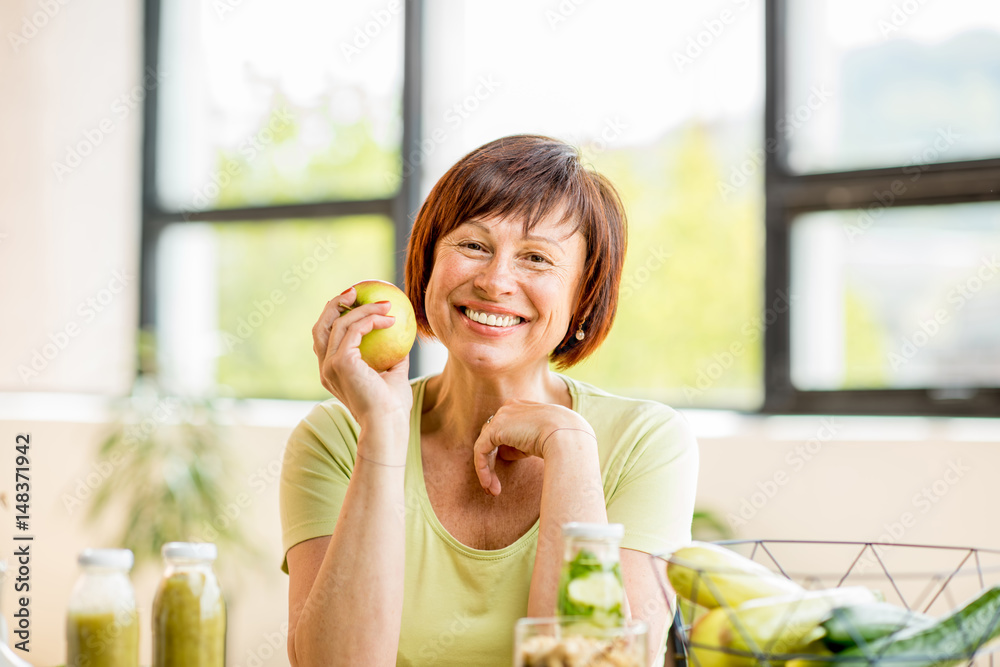 Portrait of a beautiful older woman with green healthy food on the table indoors on the window backg
