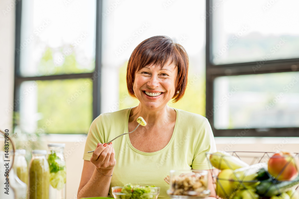 一位美丽的年长女性的肖像，室内桌子上的窗户靠背上有绿色健康食品