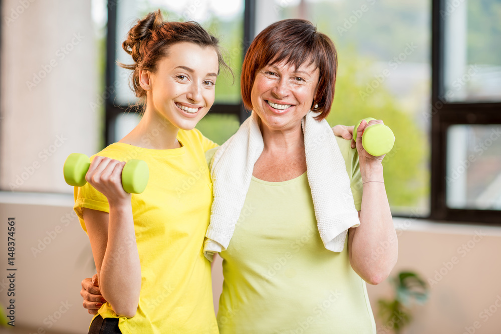 Young and older women in sportswear training with dumbbells indoors on the window background
