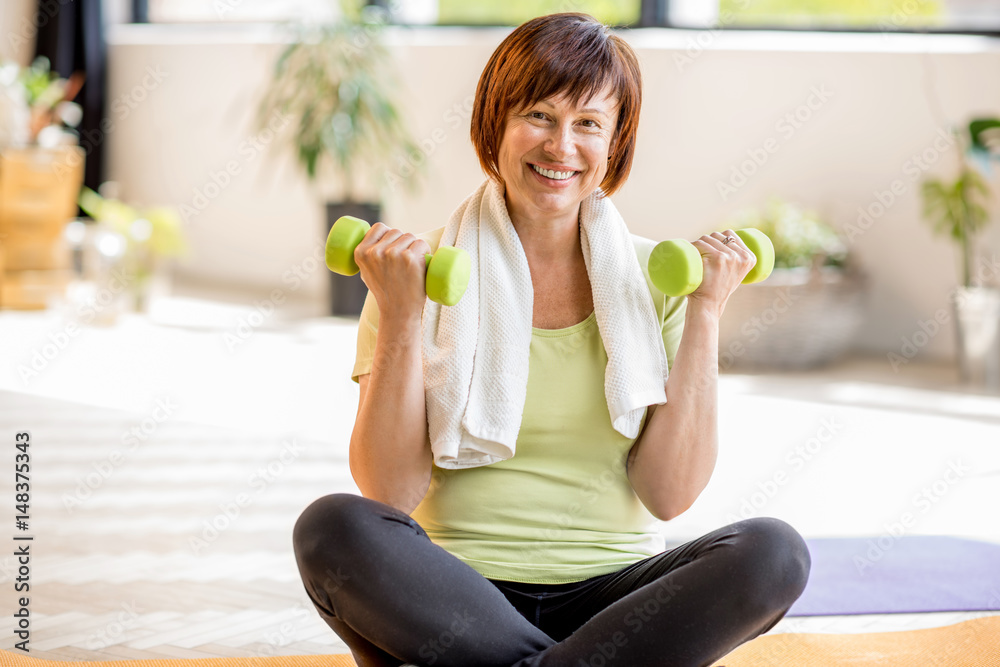 Portrait of an older woman in sportswear exercising with dumbbells indoors at home or gym