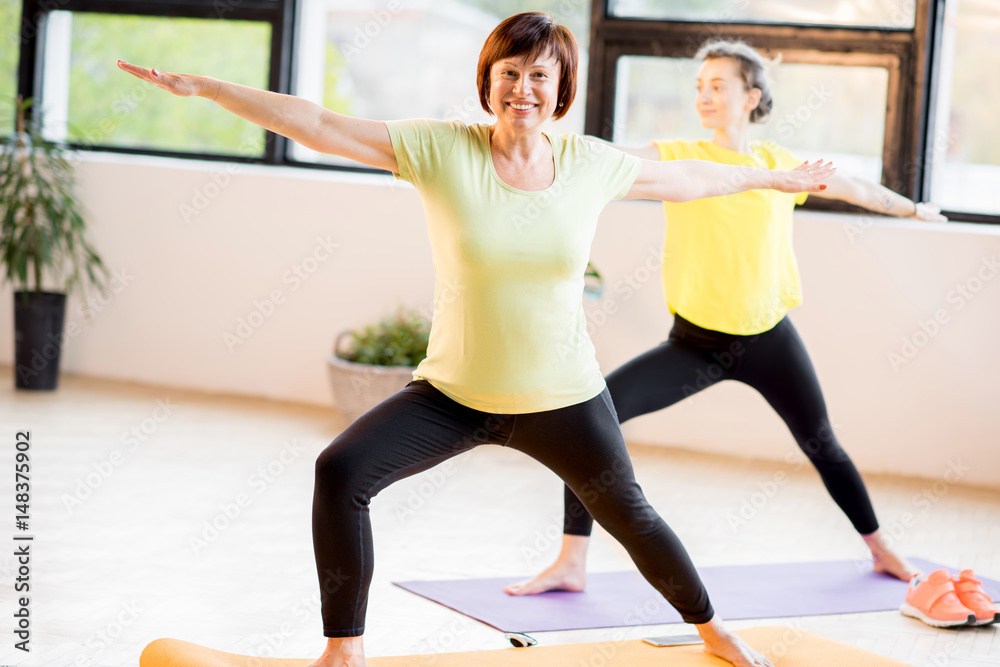 Young and older women in sports wear doing yoga together indoors at home or a gym