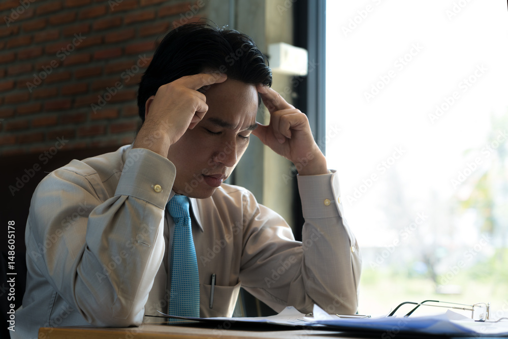 Asian businessman sitting and thinking in cafe, looking frustrated and depressed.