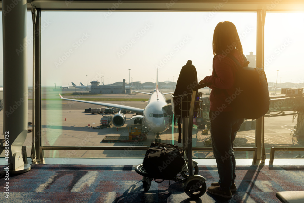 一名年轻女子在机场航站楼拿着一个手提包，飞机停在机场跑道后面