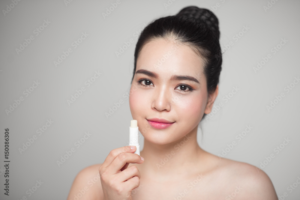 亚洲女性在灰色背景上涂抹卫生润唇膏