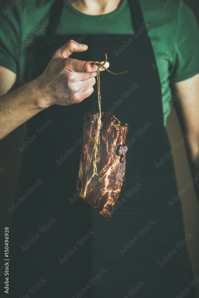 在当地农贸市场，一名身穿黑色围裙的男子手里拿着一块腌猪肉。美食家，奥尔加