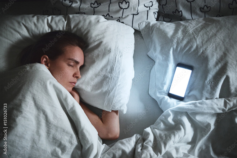 Donna dorme con smartphone accanto, stress da lavoro 