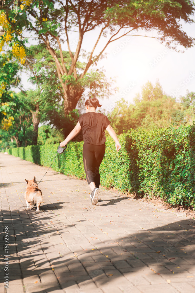 运动女孩早上带着一只狗（彭布罗克威尔士柯基犬）在路上跑步