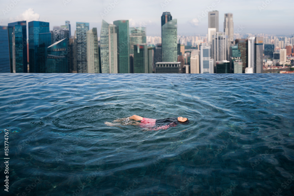 亚洲女孩在酒店屋顶游泳池游泳