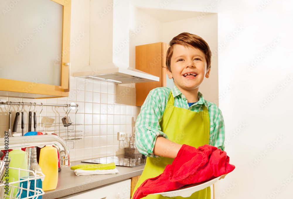快乐的小男孩用红洗碗巾擦干盘子