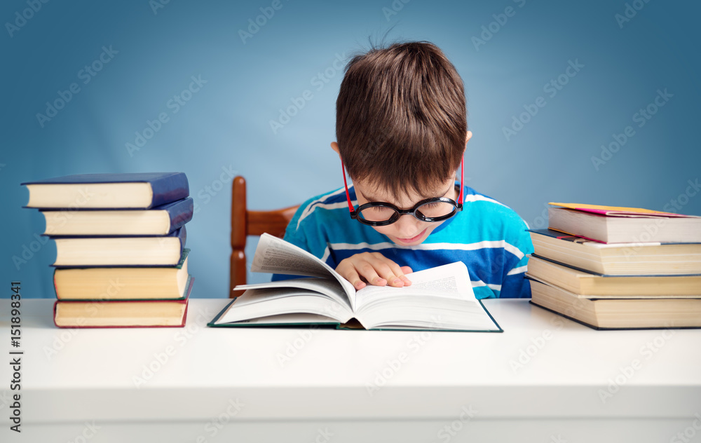 七岁的孩子在家看书。男孩在蓝色背景的桌子旁学习