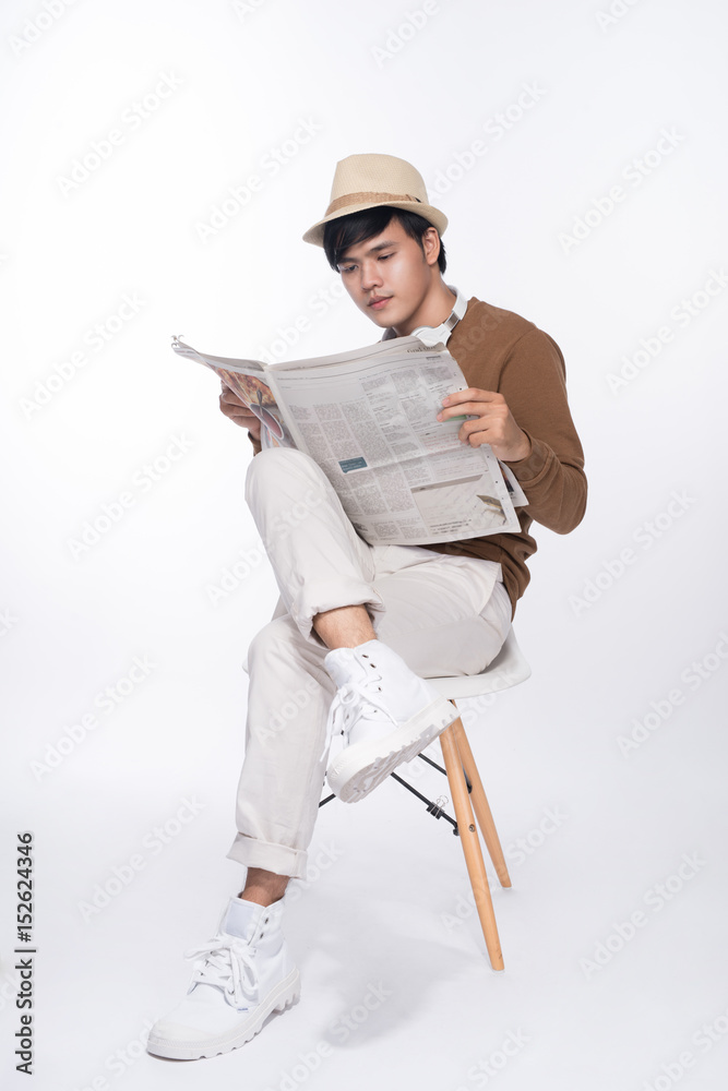 聪明休闲的亚洲男人坐在椅子上，在演播室背景下看报纸