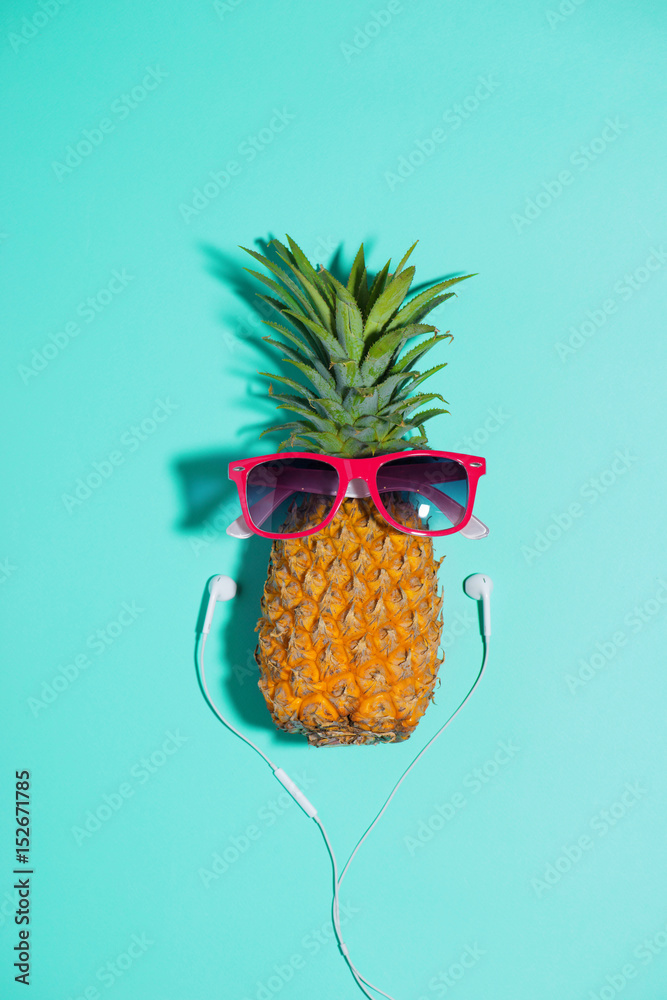 戴着太阳镜和耳机的时尚菠萝在蓝色背景下听音乐
