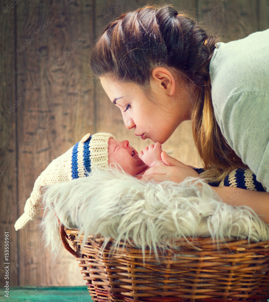 快乐的母亲和她的新生儿在一起。母性概念。穿着可爱服装的婴儿在篮子里