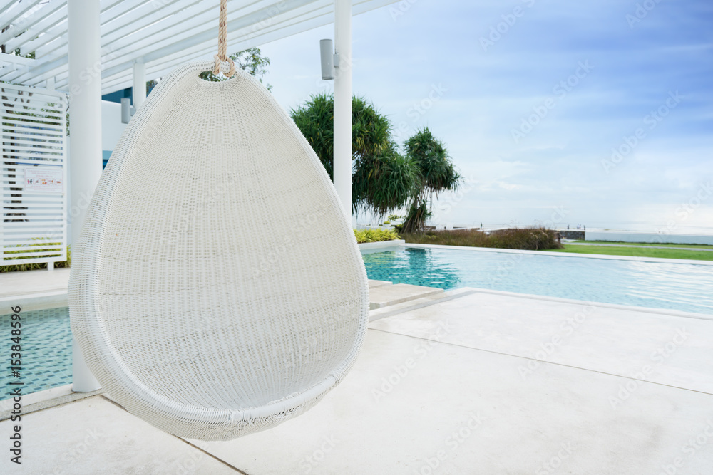 在海景游泳池放松白色藤条吊椅，度假、避暑和旅行