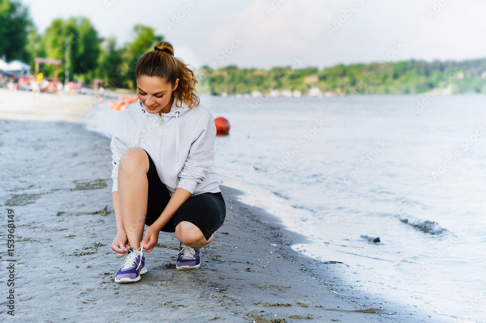 Woman lacing sport shoes and getting ready for running and exercising at beach