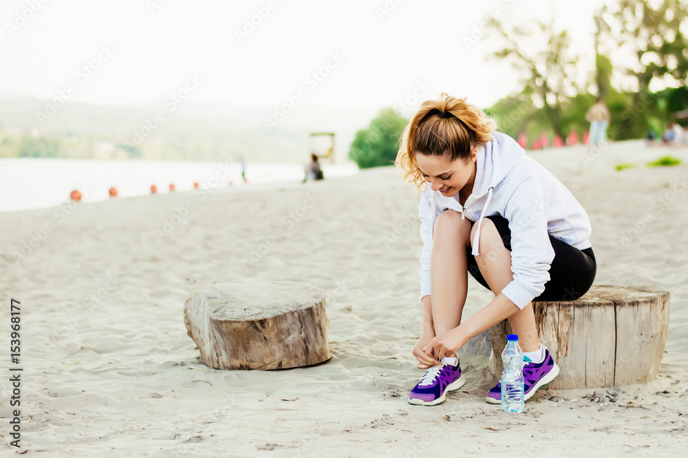 女跑步者系鞋带准备沙滩慢跑。