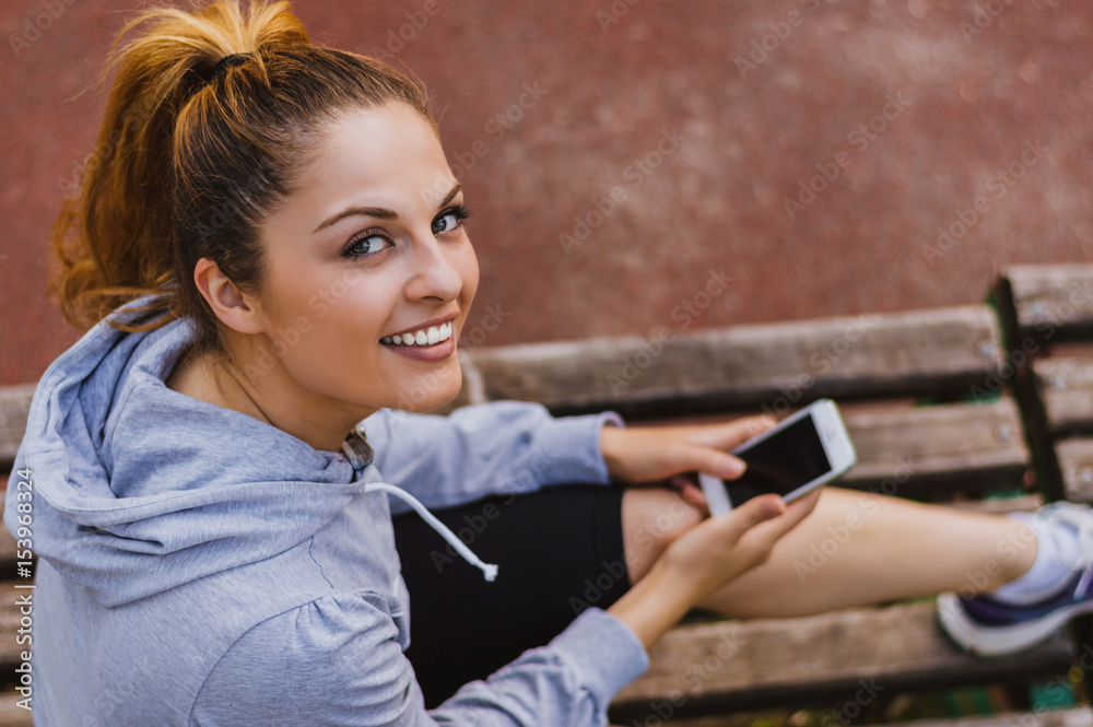 Portrait of an attractive woman using a smartphone while sitting on a wooden bench in a park