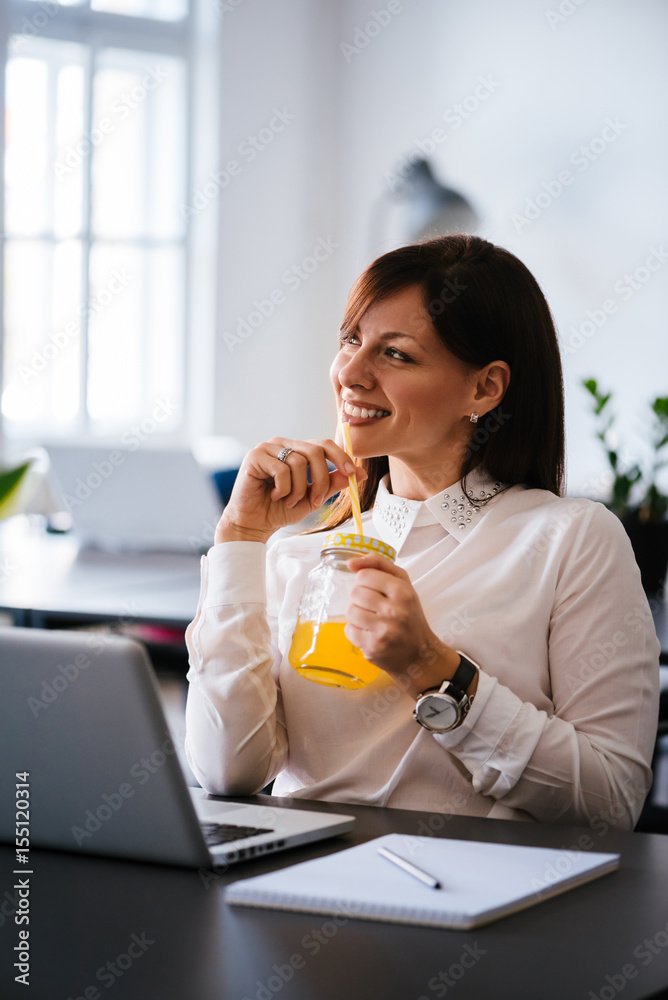 微笑优雅的女商人在明亮的办公室喝橙汁