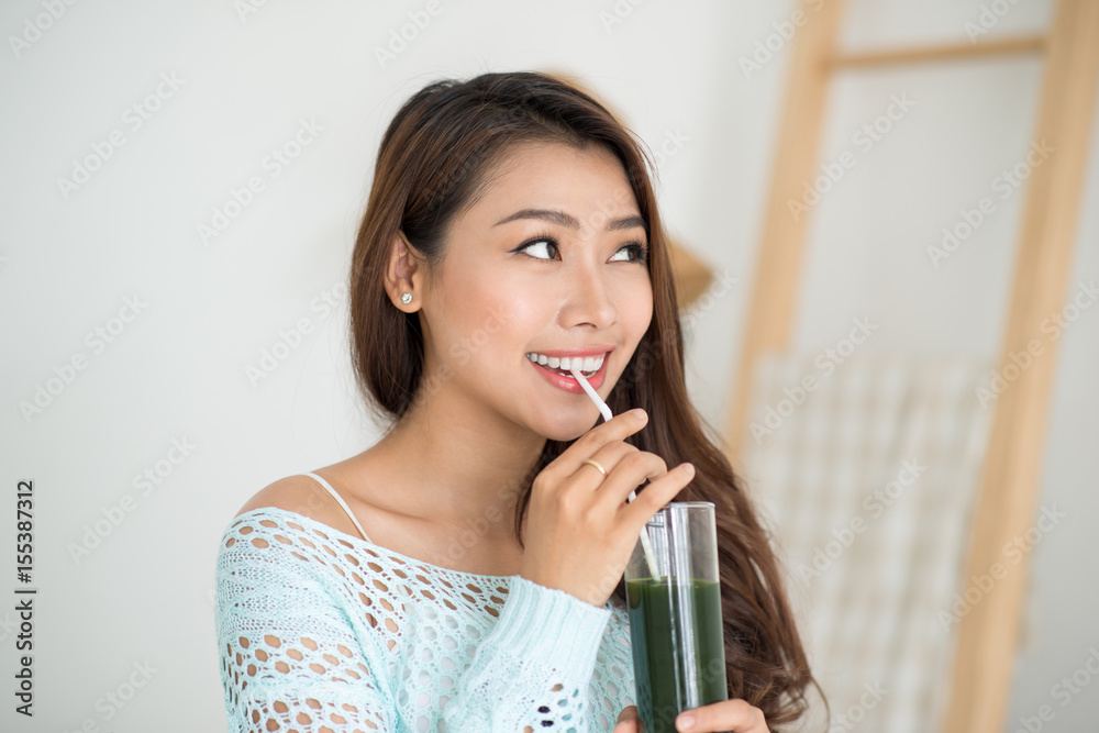 漂亮的年轻亚洲女人在家喝绿色新鲜蔬菜汁或冰沙