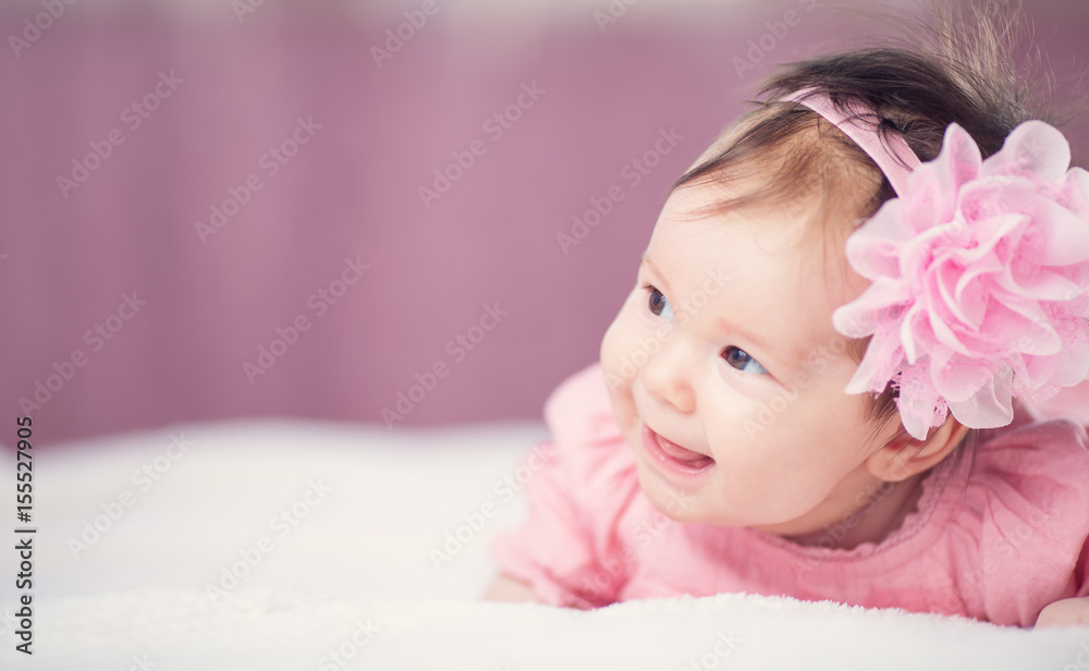 Cute little baby girl lying in the bed in pink dress. Three month old infant child on white soft bla