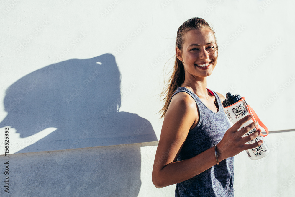 快乐的女跑步者拿着水瓶微笑