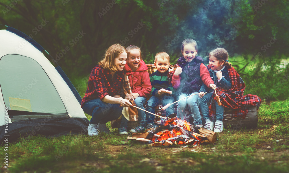 快乐的旅游家庭徒步旅行。母亲和孩子在帐篷附近的篝火上炸香肠