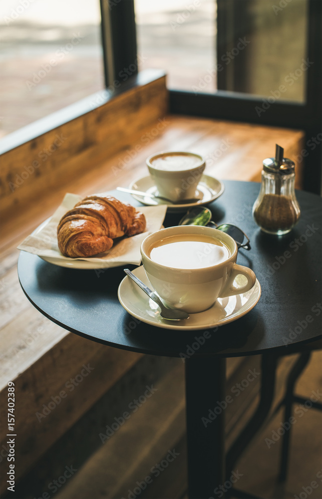咖啡馆小桌子上的咖啡拿铁、卡布奇诺和羊角面包，法国或意大利早餐概念