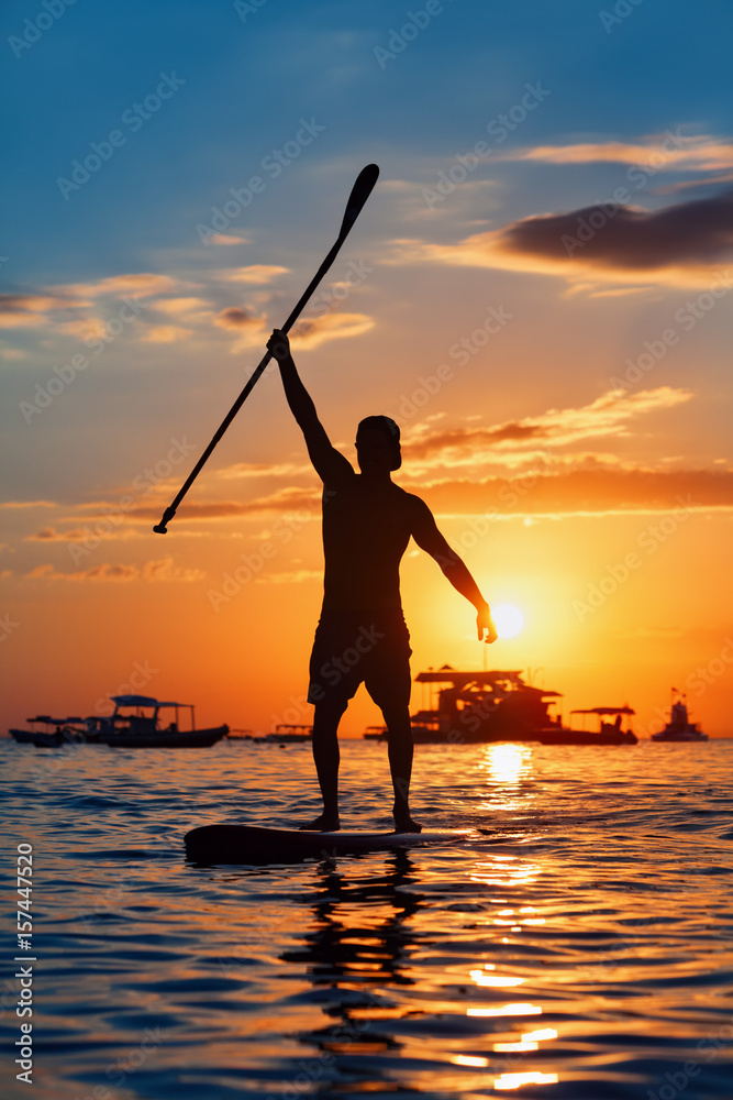 桨板运动员。年轻运动员在立式桨板上划水的黑色日落剪影。健康