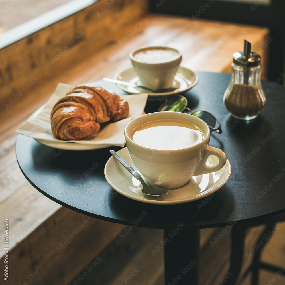 咖啡馆小桌子上的咖啡拿铁、卡布奇诺和羊角面包，法国或意大利早餐概念，