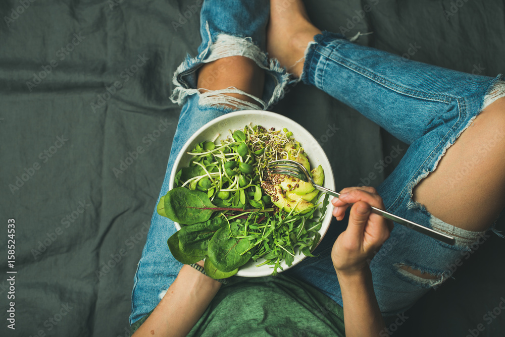 Green vegan breakfast meal in bowl with spinach, arugula, avocado, seeds and sprouts. Girl in jeans 