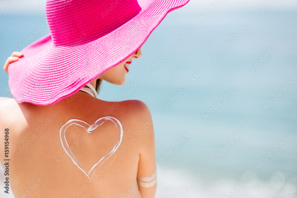 Back view on a beautiful woman in pink hat with sunscreen heart shape on her shoulder having a sunba