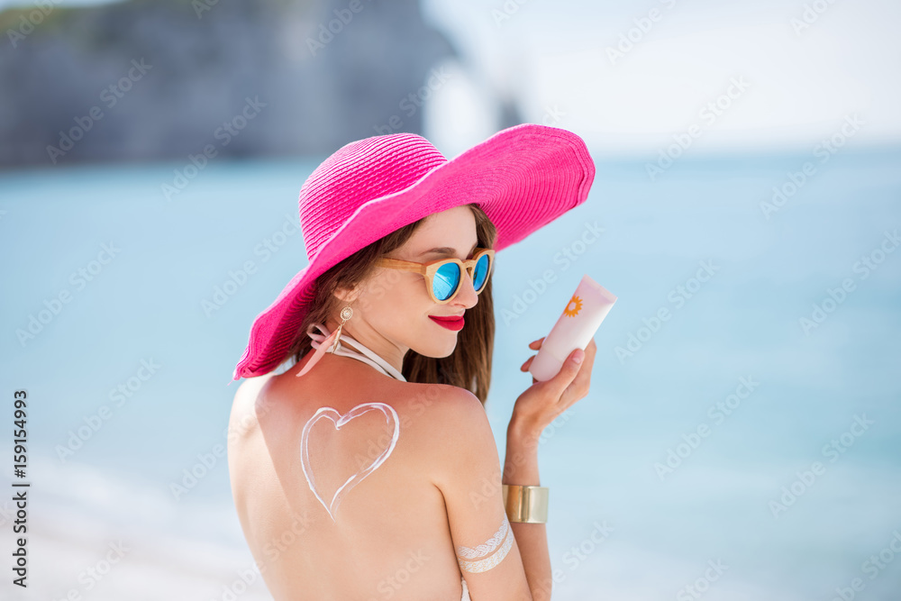 Portrait of a beautiful smiling woman in pink hat with sunscreen heart shape on her shoulder holding