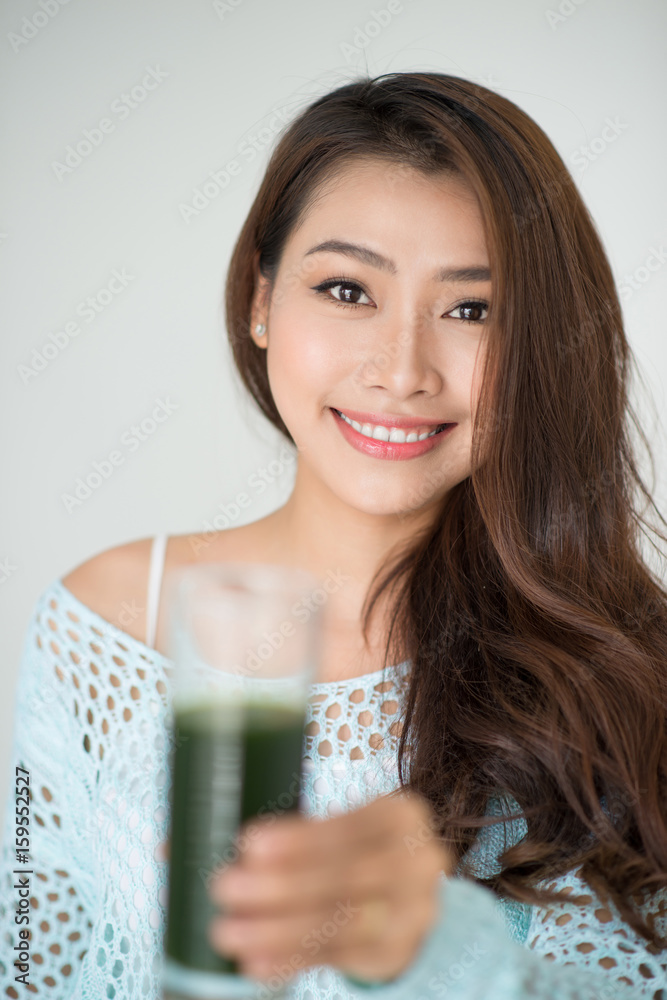 漂亮的年轻亚洲女人在家喝绿色新鲜蔬菜汁或冰沙