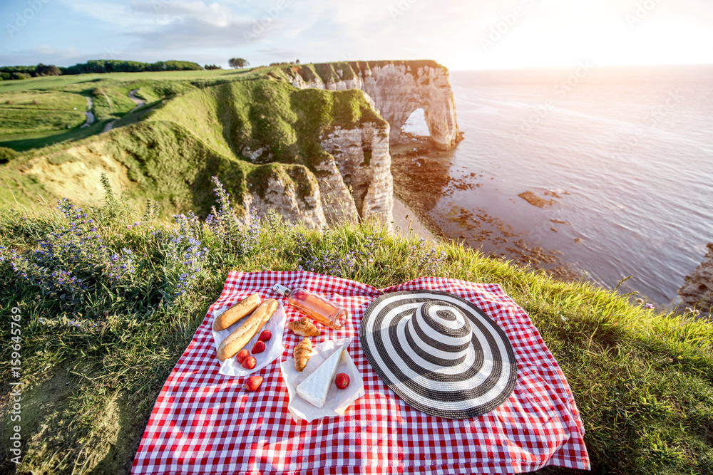 Picnic with french food on the checkered tablecloth on the beautiful rocky coastline background