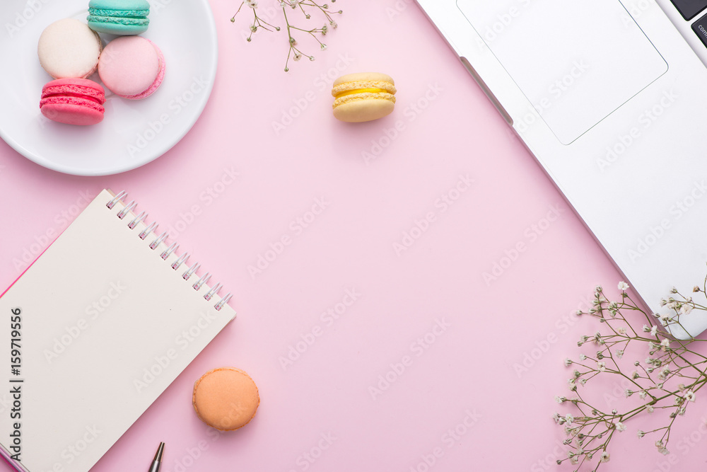 Flatlay of laptop, cake macaron and cup of tea on pink table. Beautiful breakfast with macaroon.