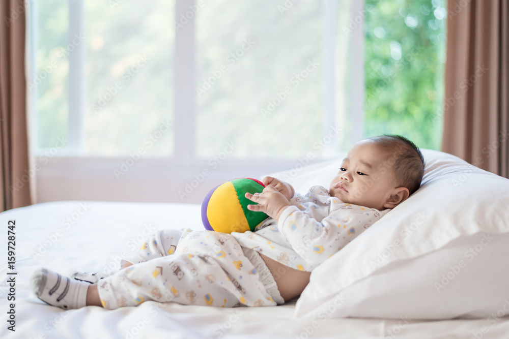 亚洲可爱的男婴在家里阳光明媚的白色卧室里玩五颜六色的彩虹球玩具。