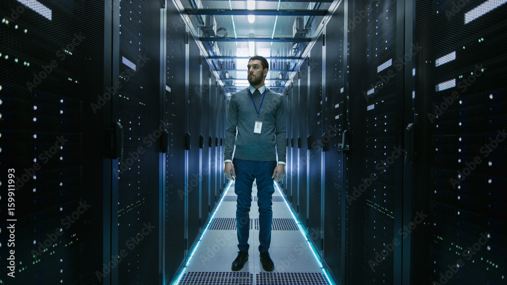 古玩IT工程师站在工作数据中心服务器室的中央。