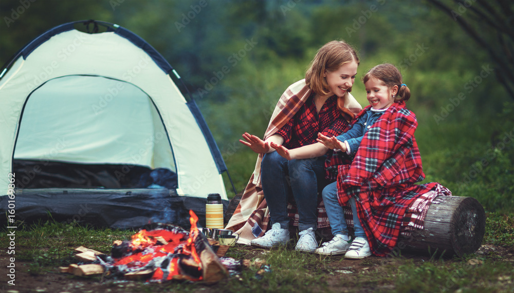 家庭母女带着帐篷露营，在篝火旁温暖双手