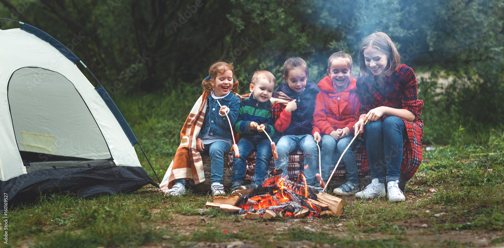Happy tourist family on journey hike. mother and children fry sausages on bonfire near tent