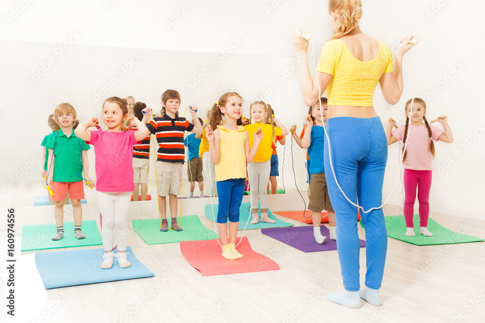 Group of happy kids jumping ropes at gym lesson