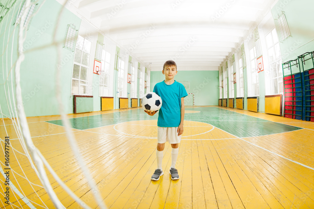男孩拿着足球站在学校体育馆里
